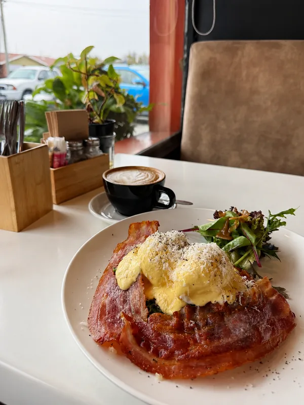 Bacon eggs Benedict, salad and a coffee on a table by the cafe window