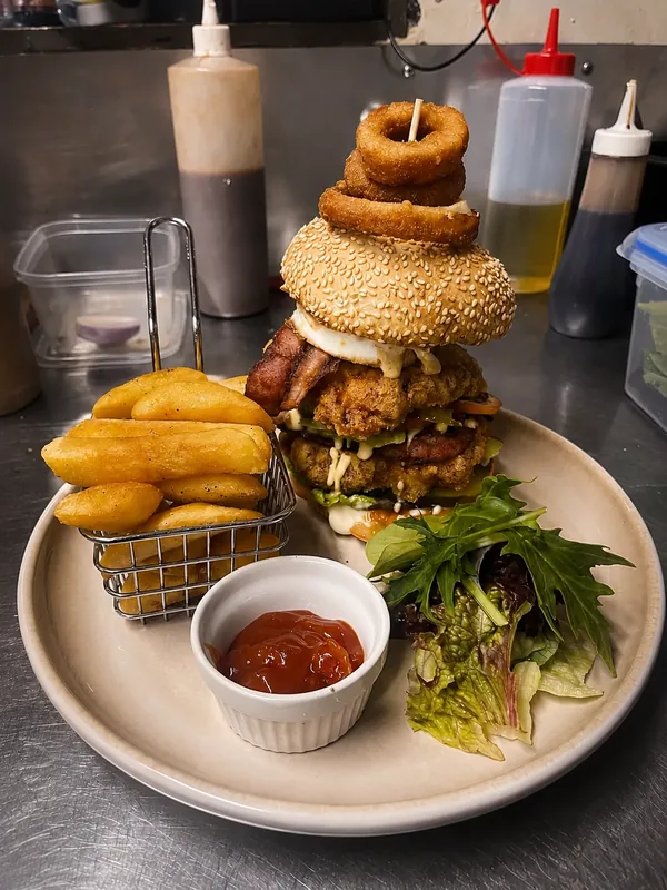 A stacked burger with onion rings, fries and salad